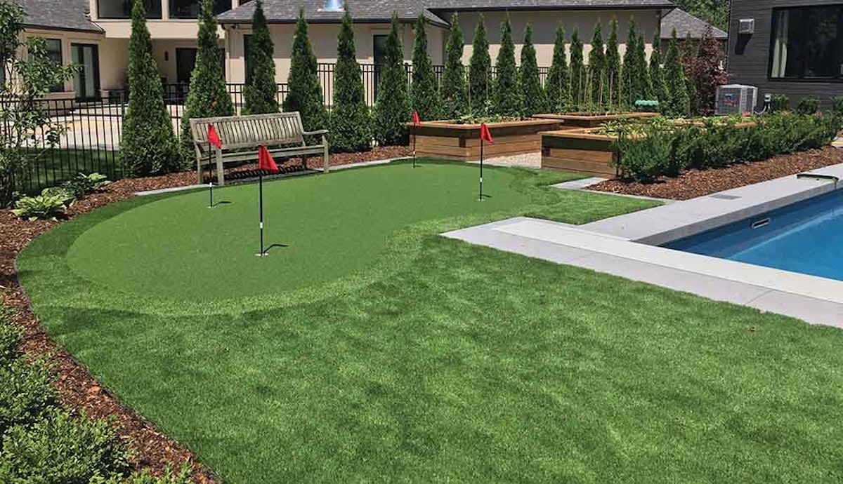 A backyard with a putting green and a pool.