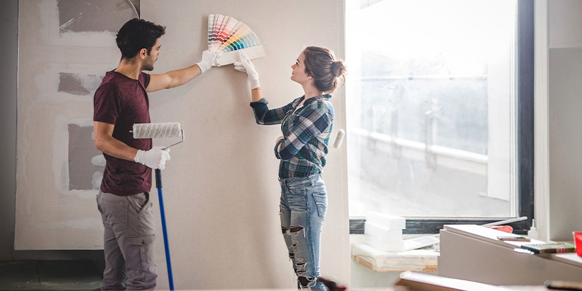 A man and woman painting a wall in a home.