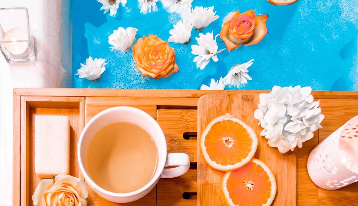 A cup of tea and orange flowers on a wooden tray.