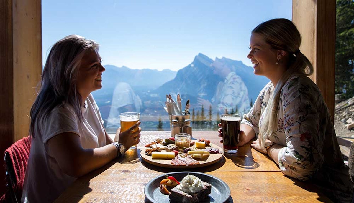 Two women sitting at a table with beer and food.