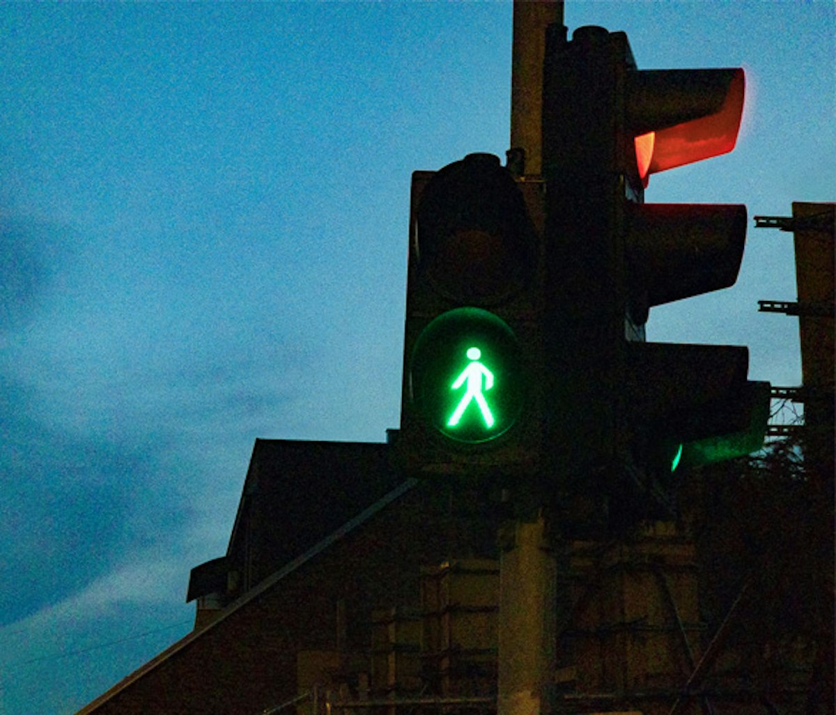 Green pedestrian traffic light signal against a dusk sky.