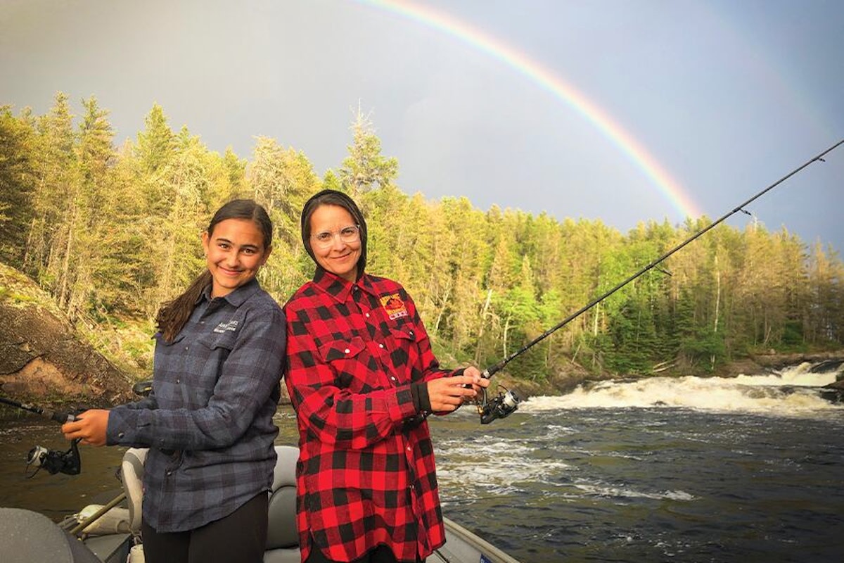 Two women fishing on a boat with a rainbow in the background.