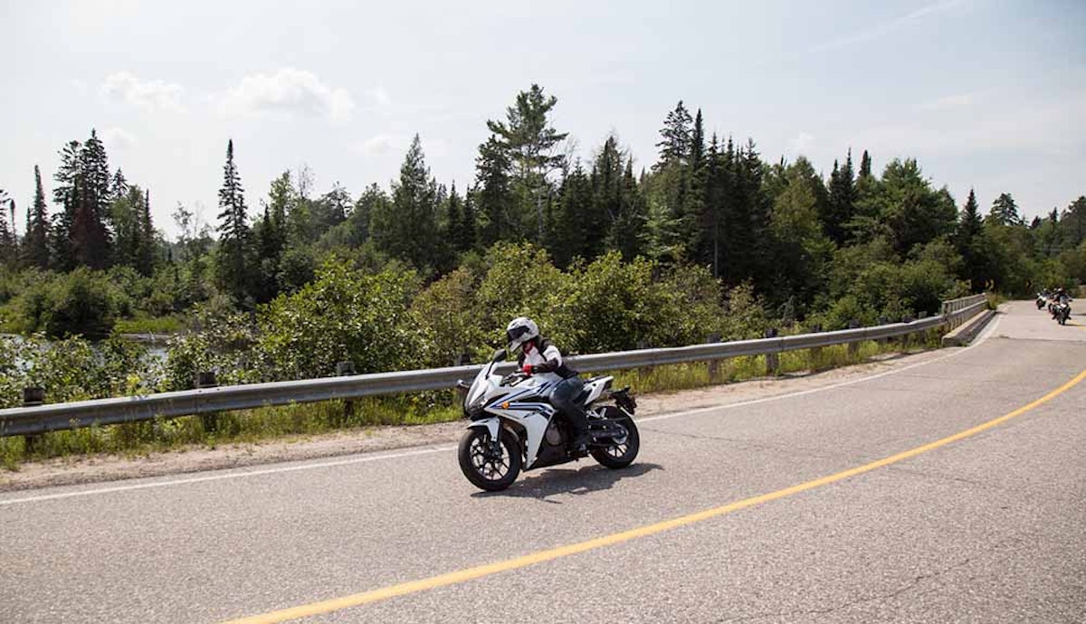 A person riding a motorcycle down a road with trees in the background.