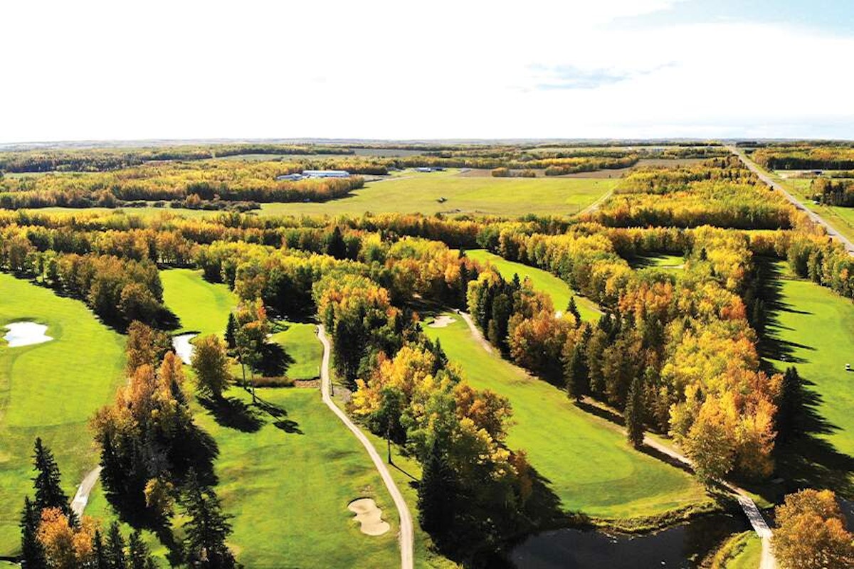 Aerial view of a lush golf course with autumn-colored trees and ponds, surrounded by a rural landscape.