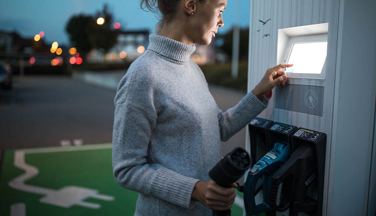 A woman is using an electric car charging station at night.