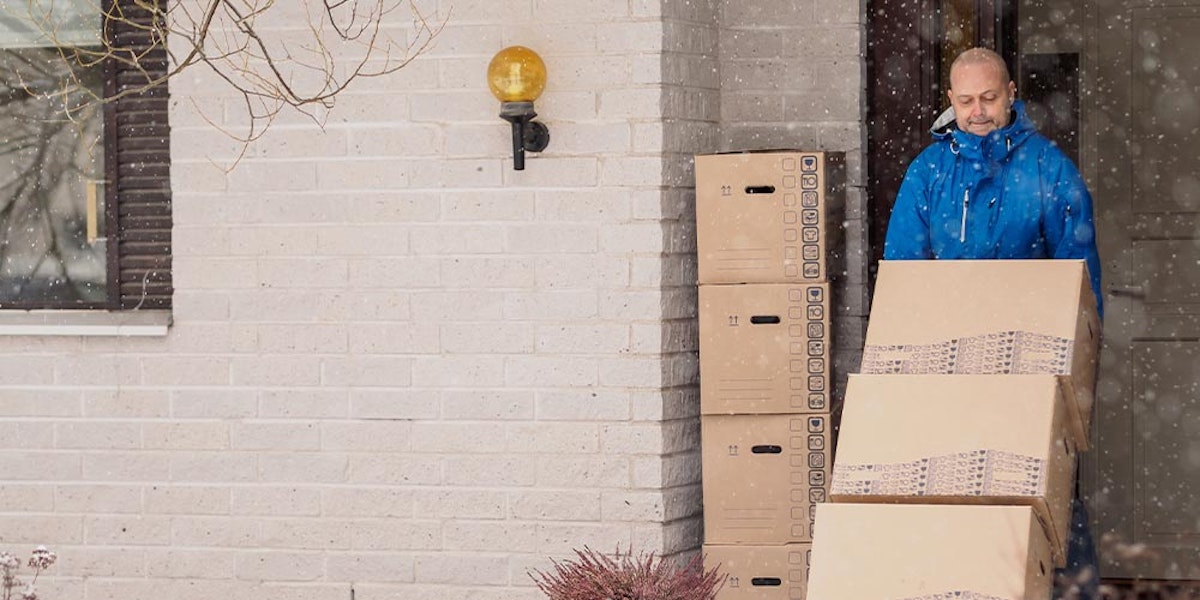 A man in a blue jacket with boxes in front of a house.