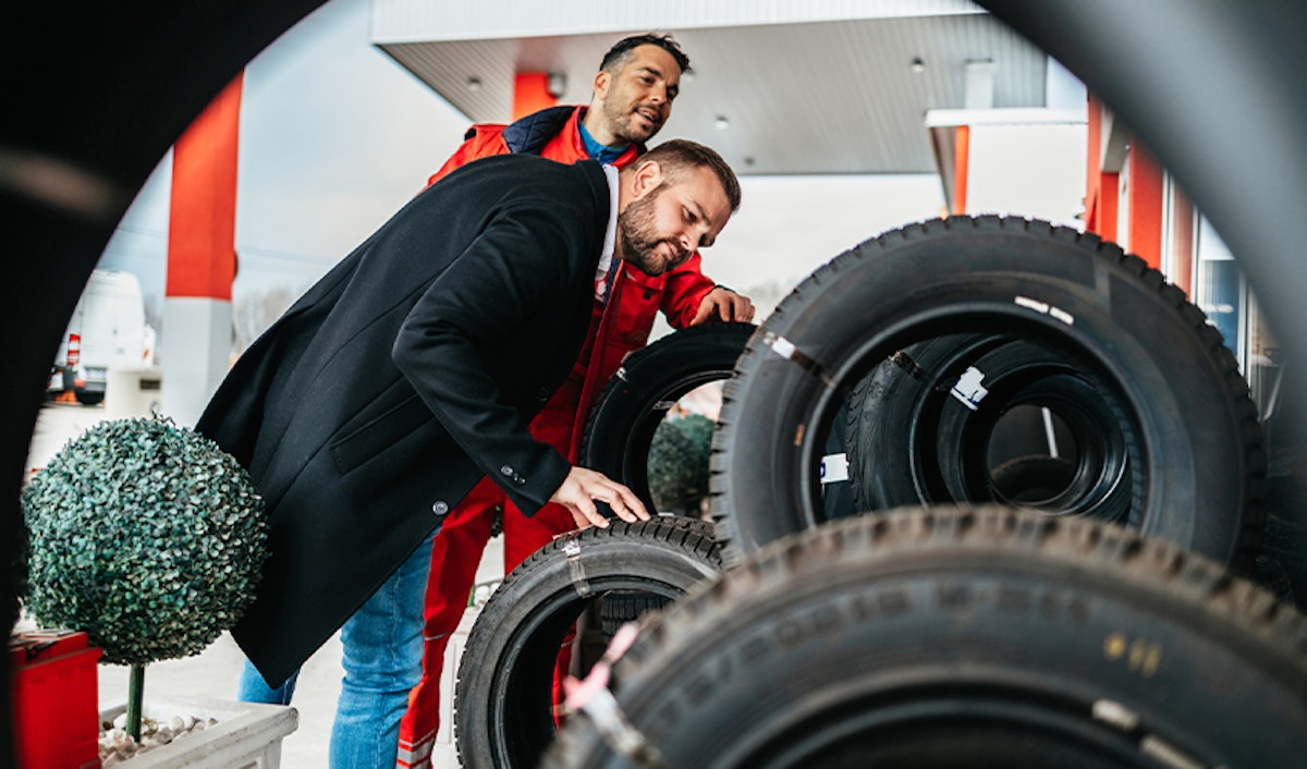Two men looking at tires at a gas station.
