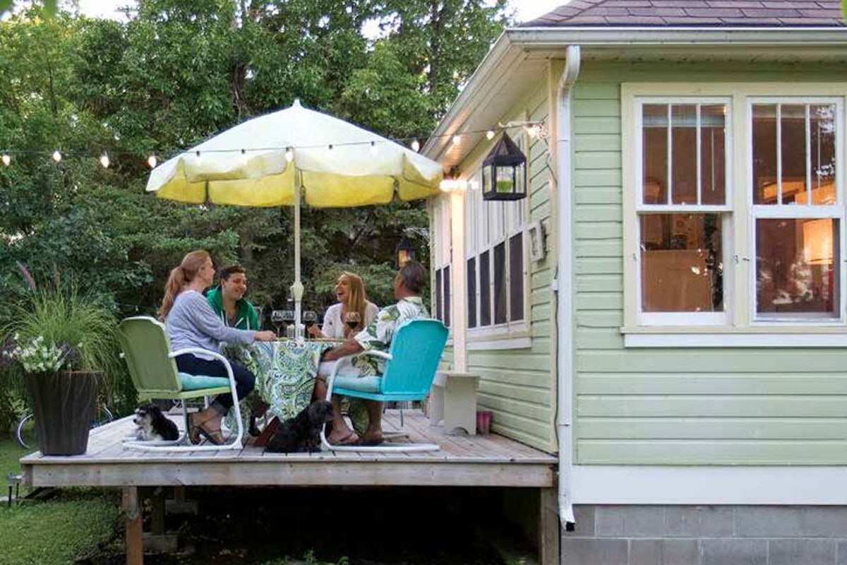 A group of people sitting on a deck in front of a green house.