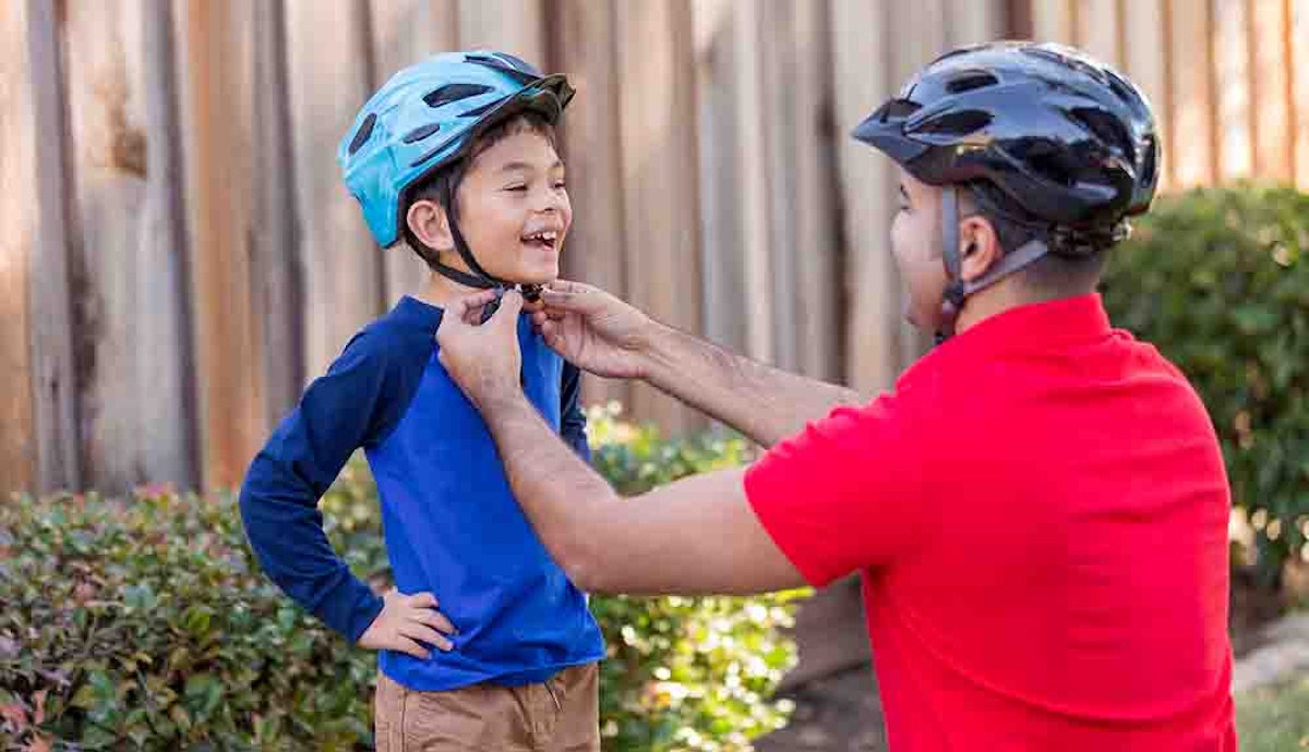 A man putting on a child's bike helmet.