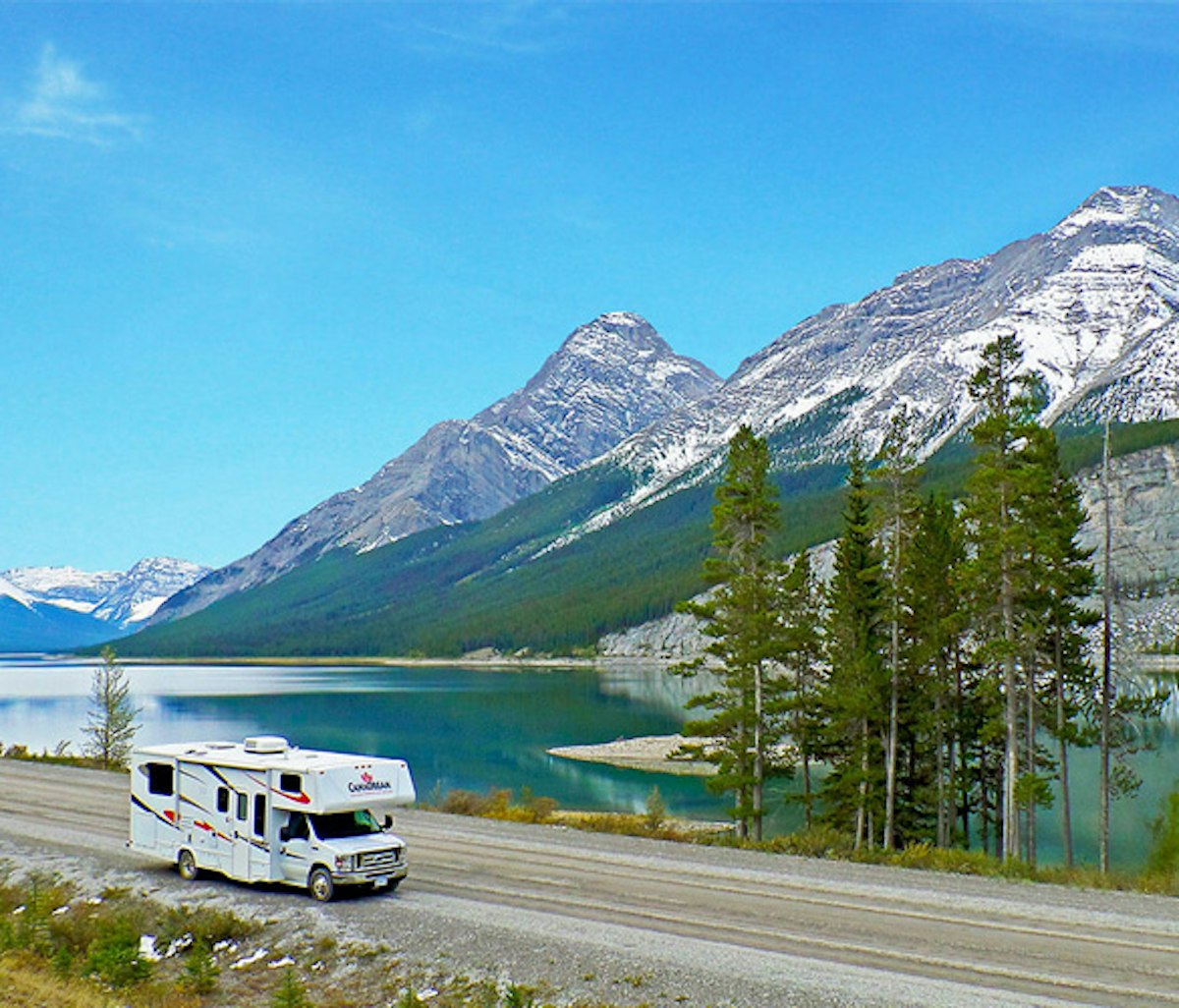 A motorhome traveling alongside a mountainous lake landscape.