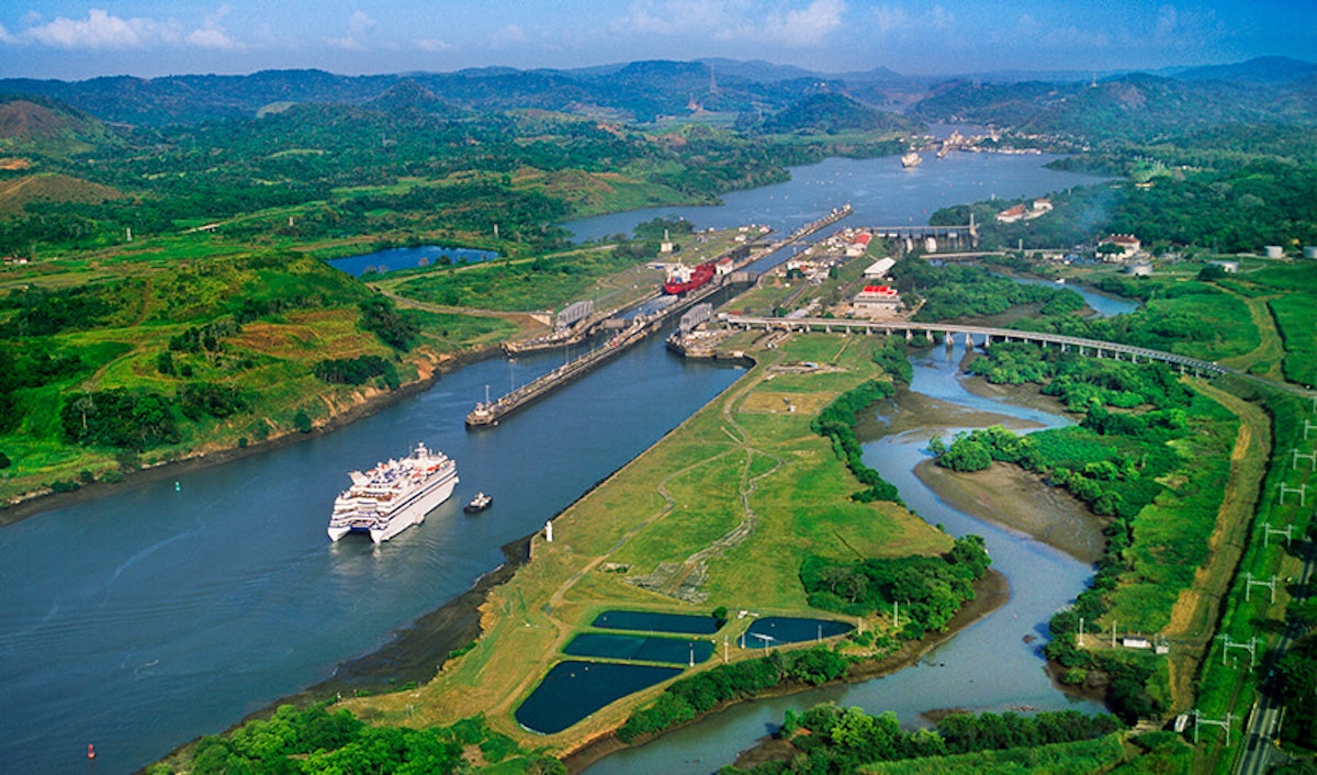 Aerial view of a large ship passing through the locks of the panama canal, with surrounding greenery and waterways.