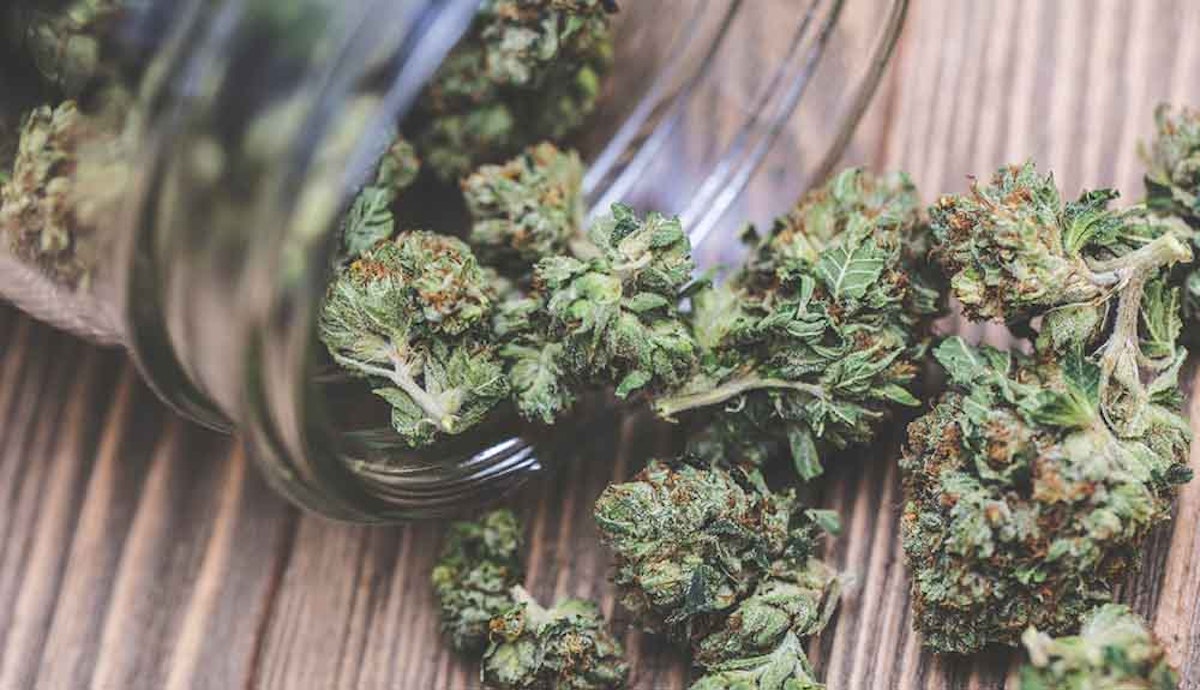 Cannabis in a glass jar on a wooden table.