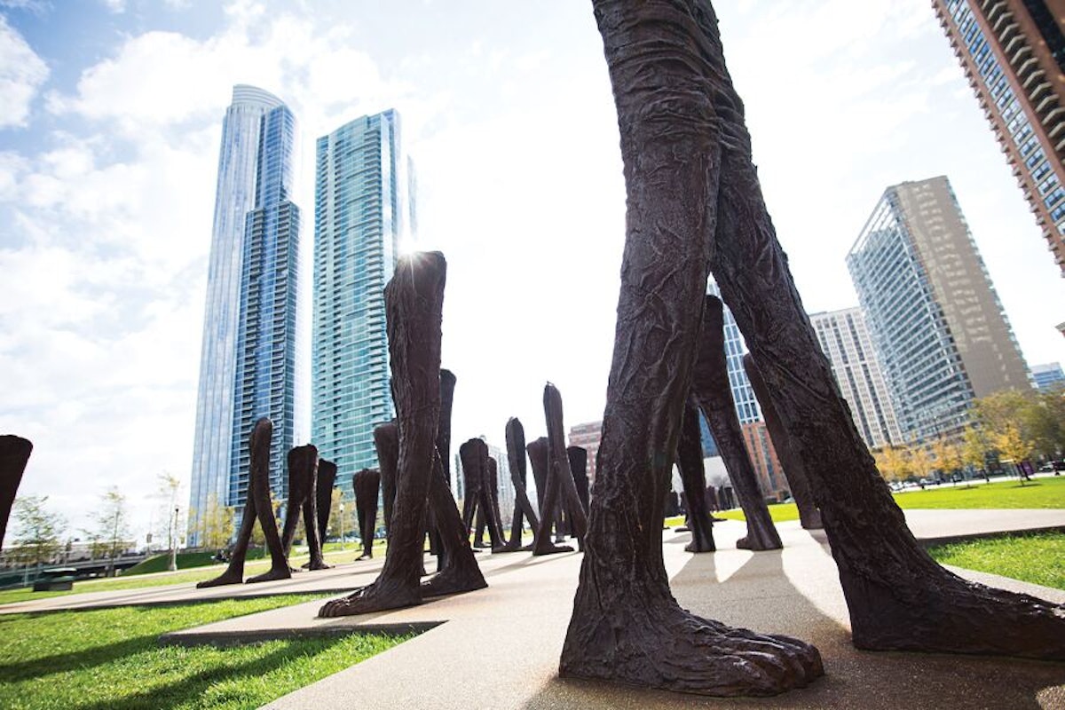 A group of sculptures in a park with tall buildings in the background.