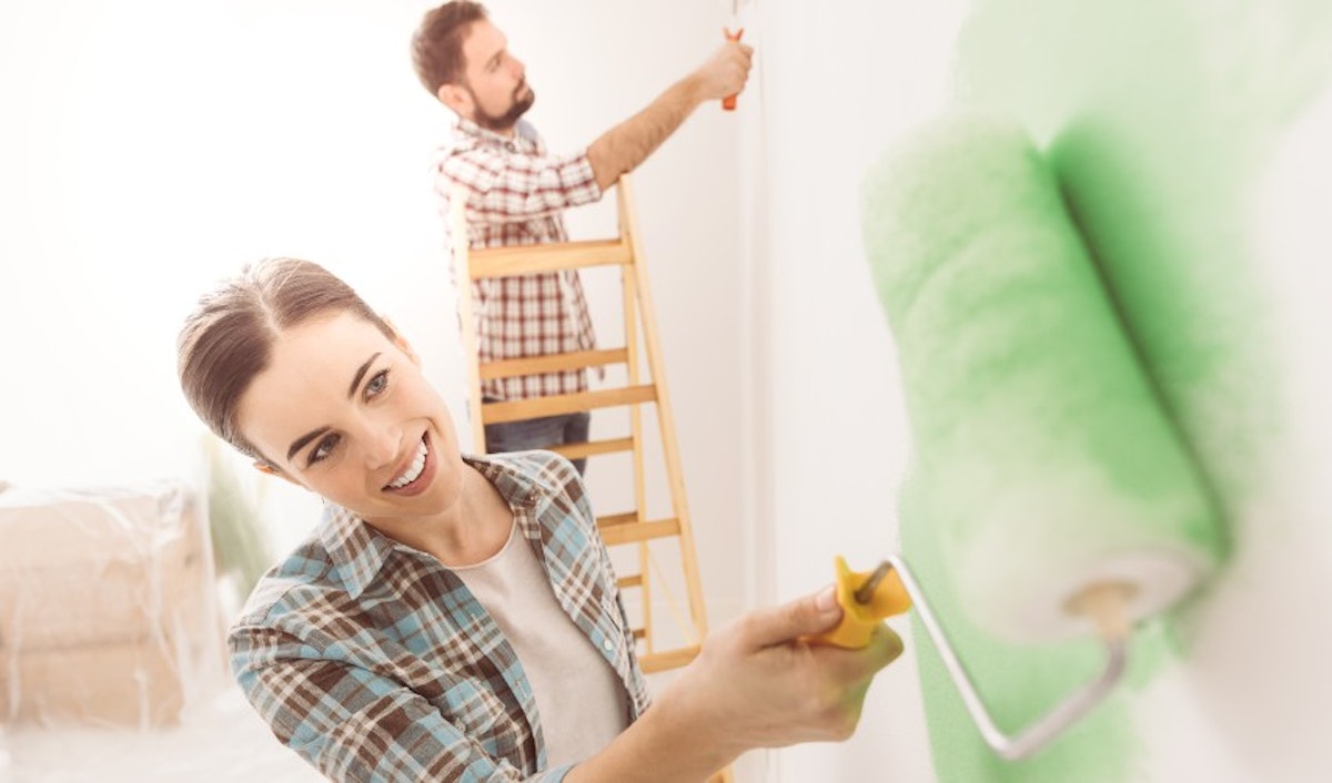 A man and woman painting a room with green paint.