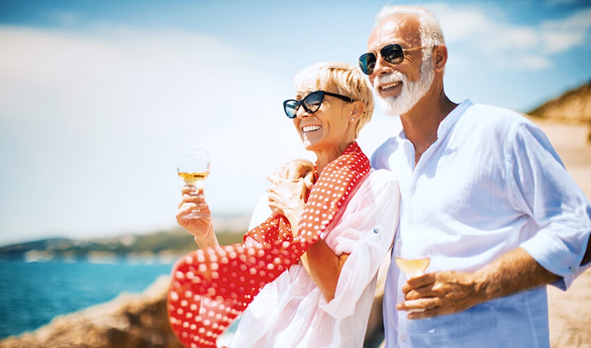 An older couple holding wine glasses on the beach.