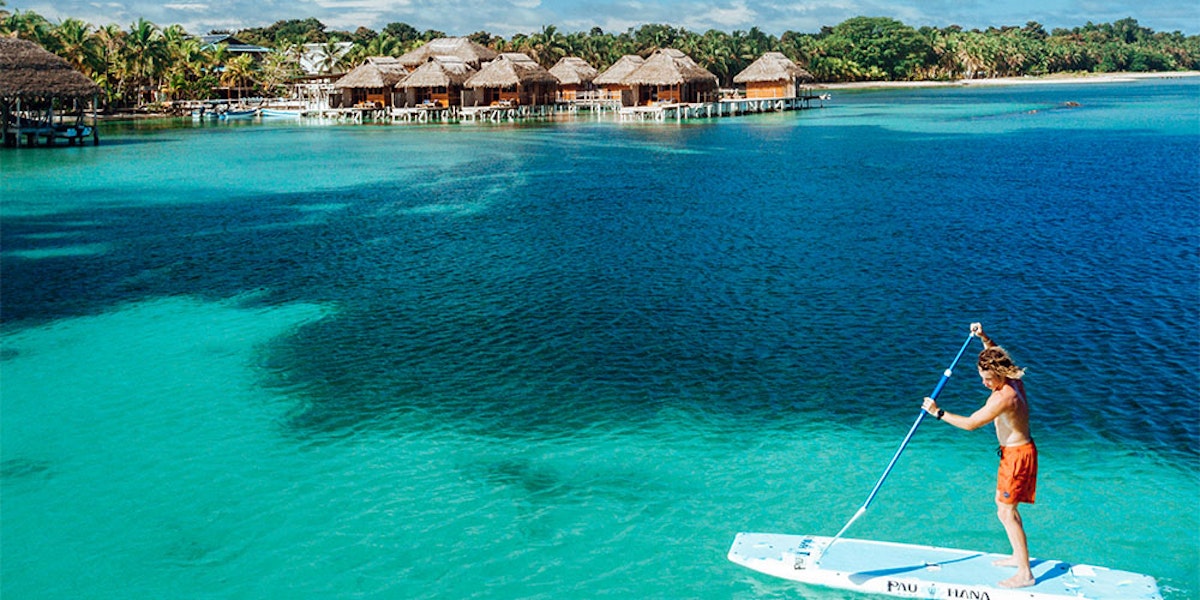 A person paddleboarding near overwater bungalows in a tropical location.
