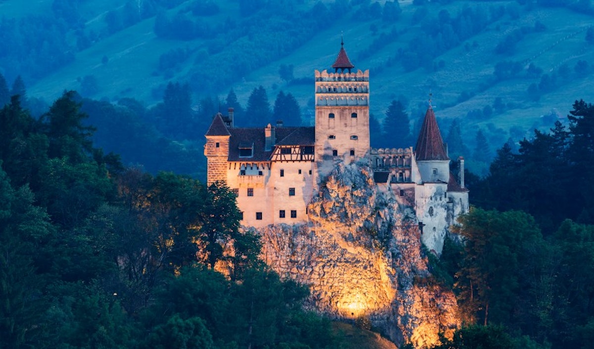 An illuminated medieval castle perched on a hillside against a twilight sky.