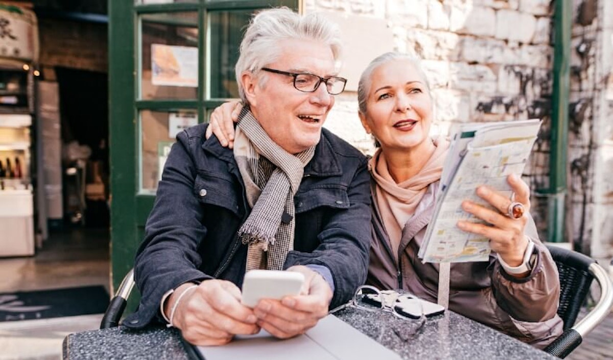 An older couple looking at a map while sitting at an outdoor table.