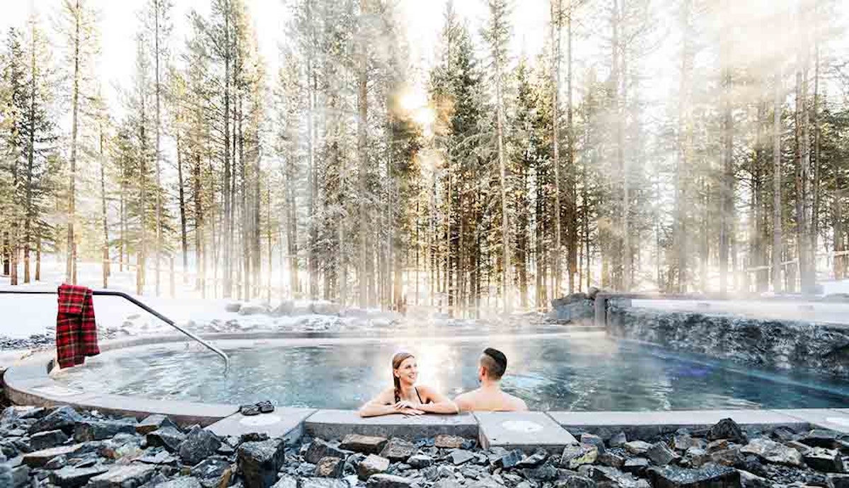 Two people sitting in a hot tub in the snow.