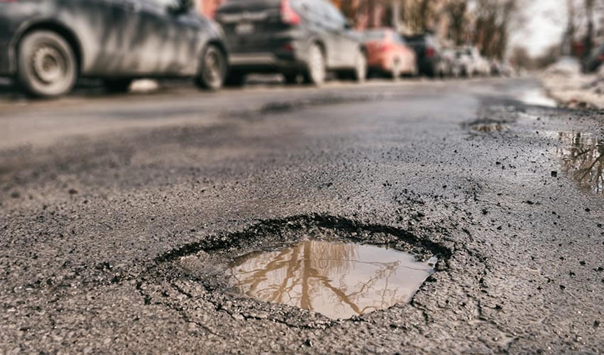 A hole in the road with cars parked around it.