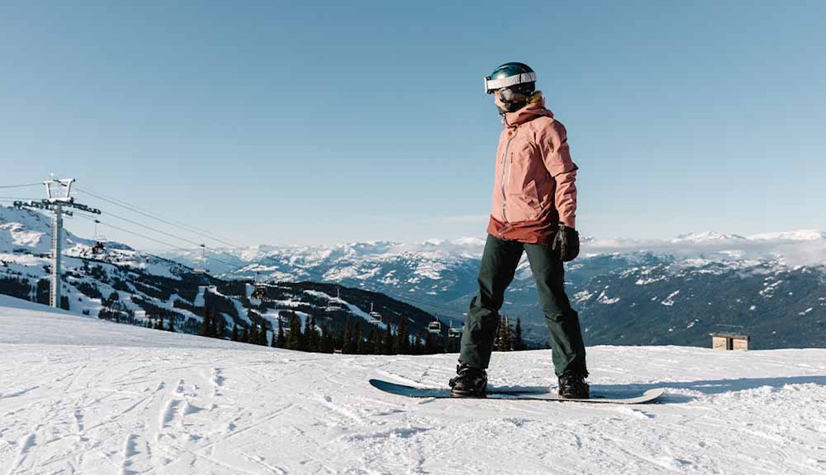 A snowboarder standing on a snow covered slope.