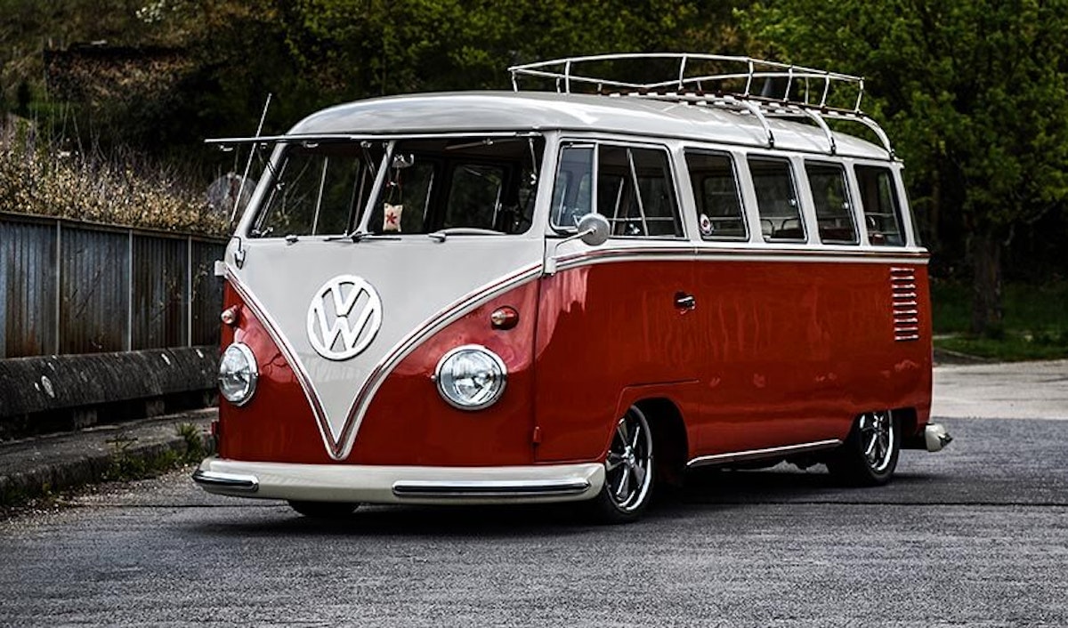 A red and white vw bus is parked on the side of the road.