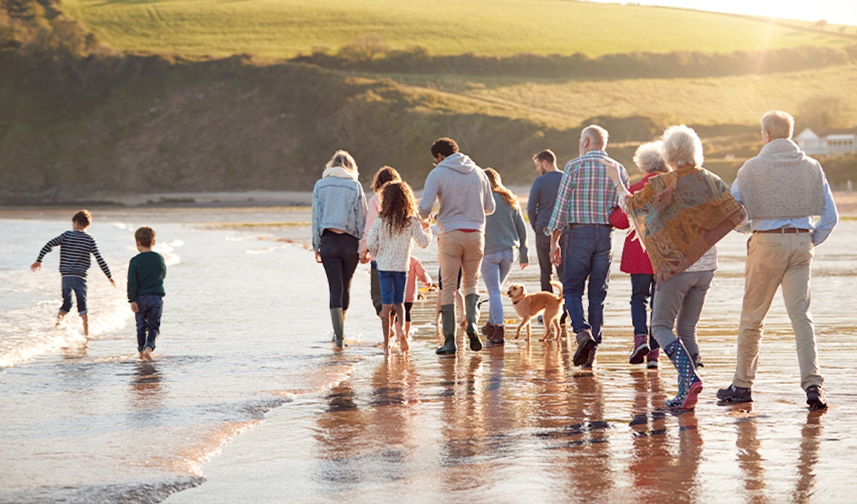 A multi-generational family walking along a beach at sunset.