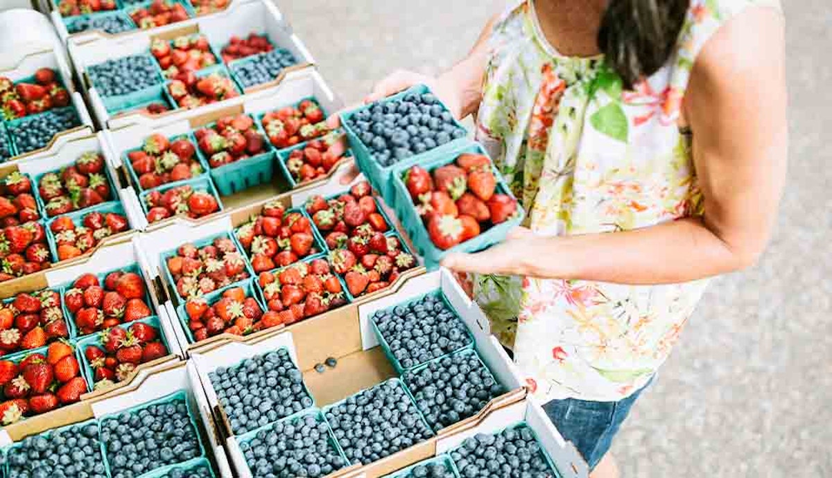 A woman is picking berries from boxes at a farmer's market.