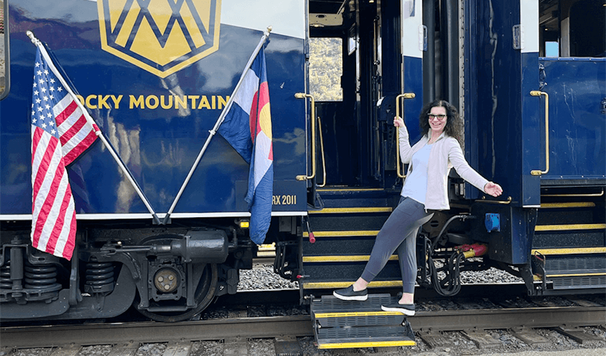 A woman standing on the steps of a blue train with an american flag.