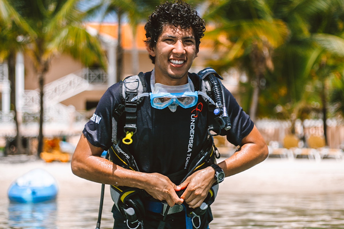 A smiling diver in full gear standing on a beach.