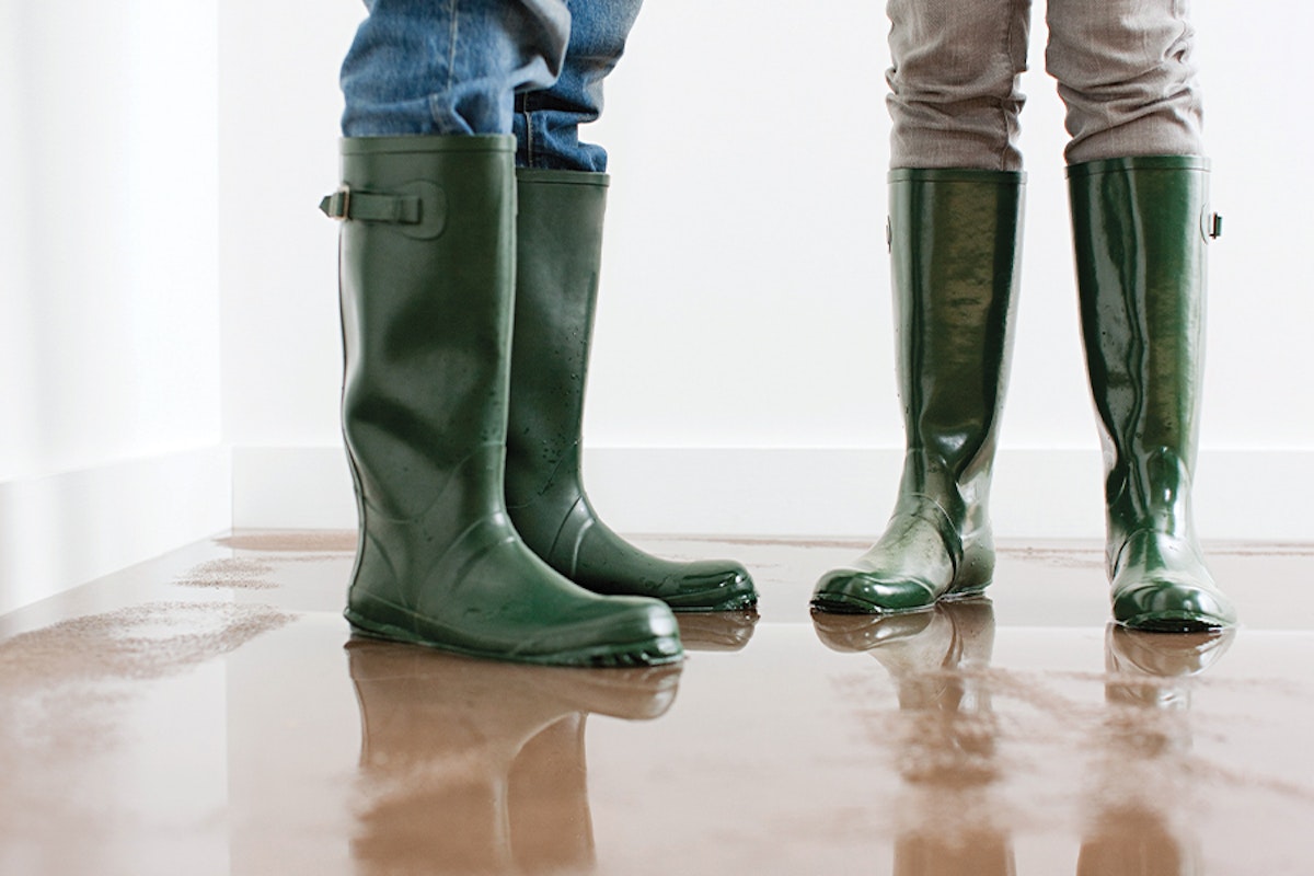 Two people in green rain boots standing in a flooded room.