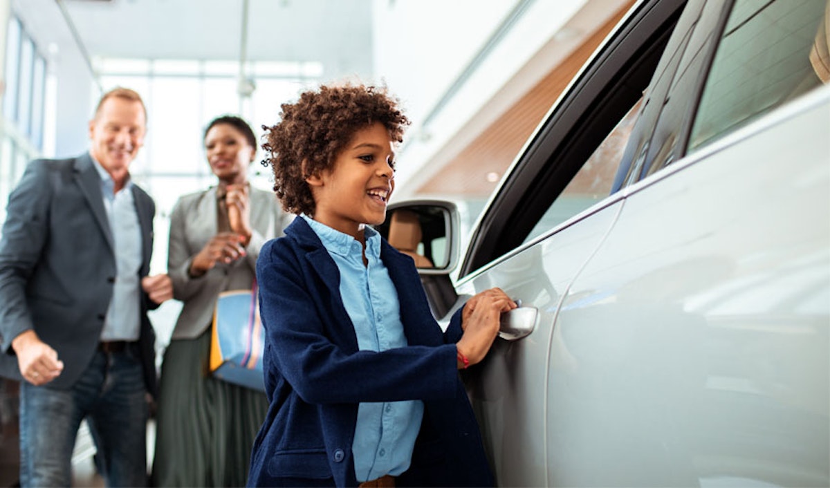 A young boy is opening the door of a car in a showroom.