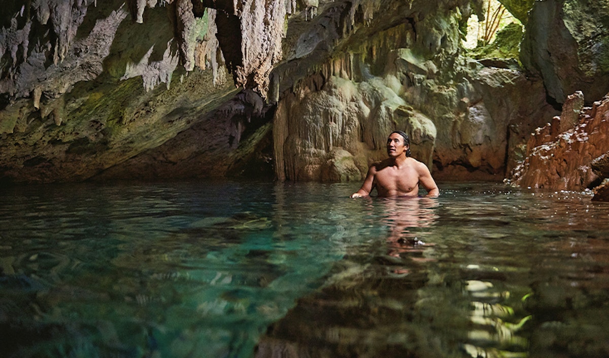 Man wading in the clear waters of a sunlit cavern.