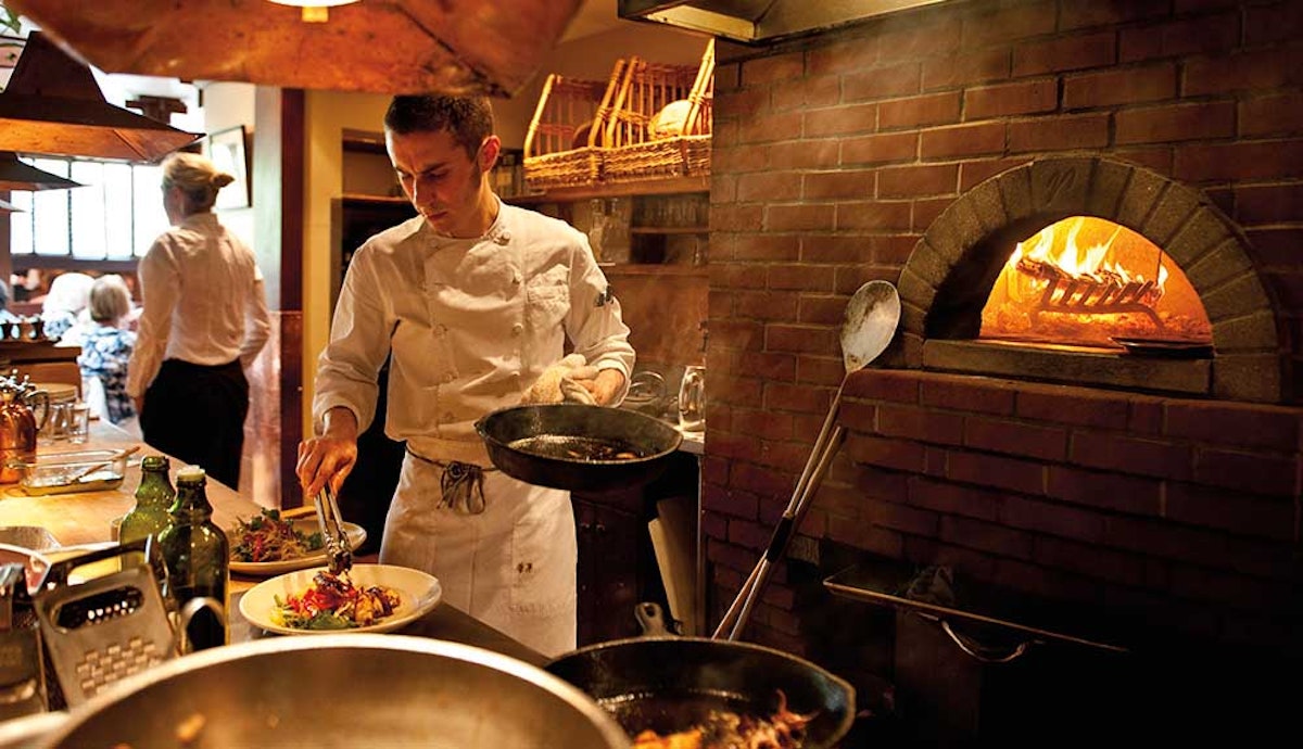 A chef preparing food in a restaurant with a brick oven.
