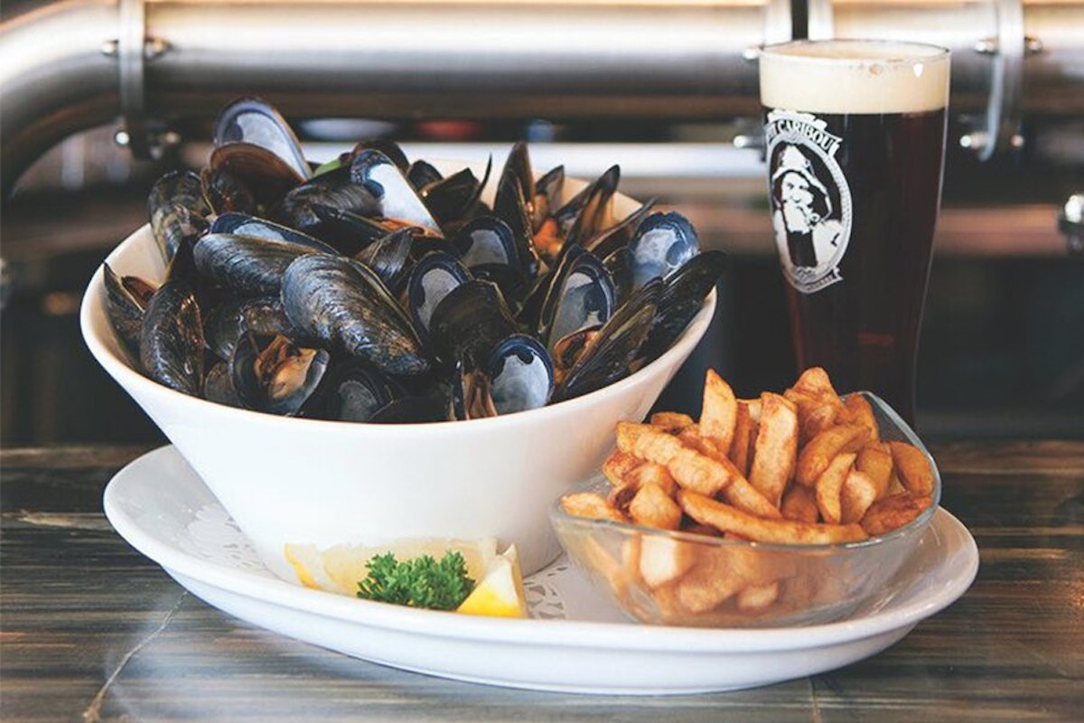 A bowl of mussels, fries and a beer on a table.