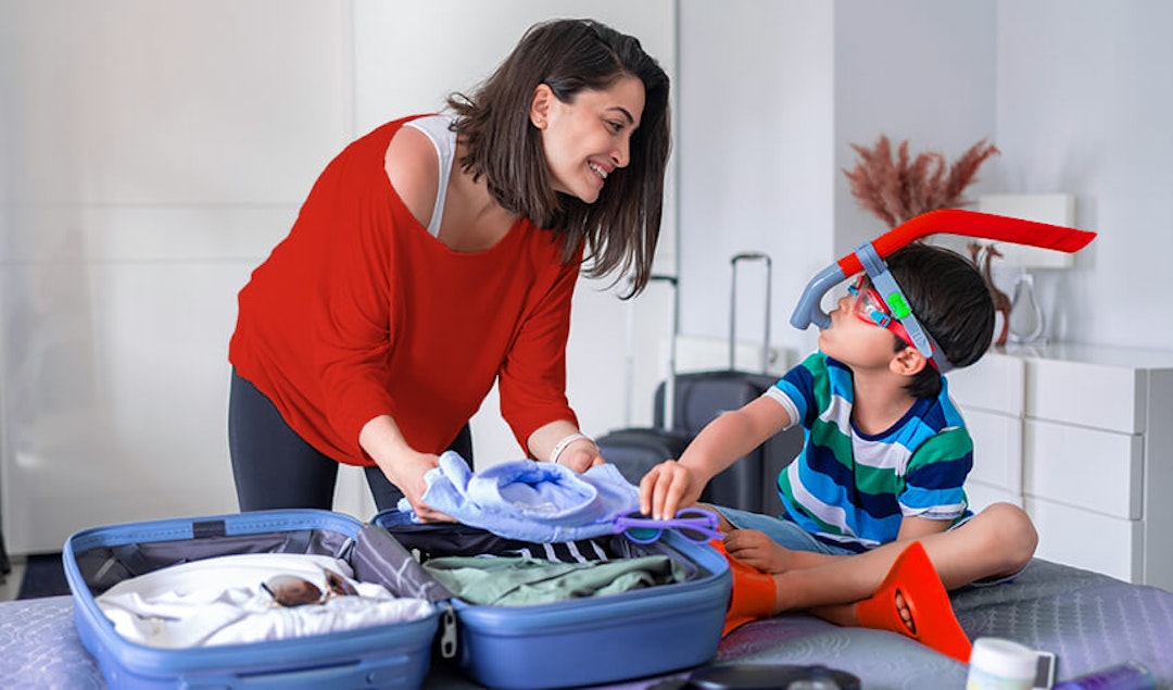 Woman and child packing a suitcase with playful snorkeling gear on.