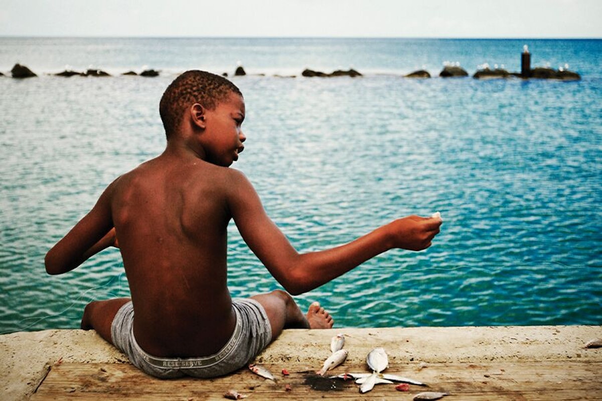 A boy sits on a dock watching the ocean.