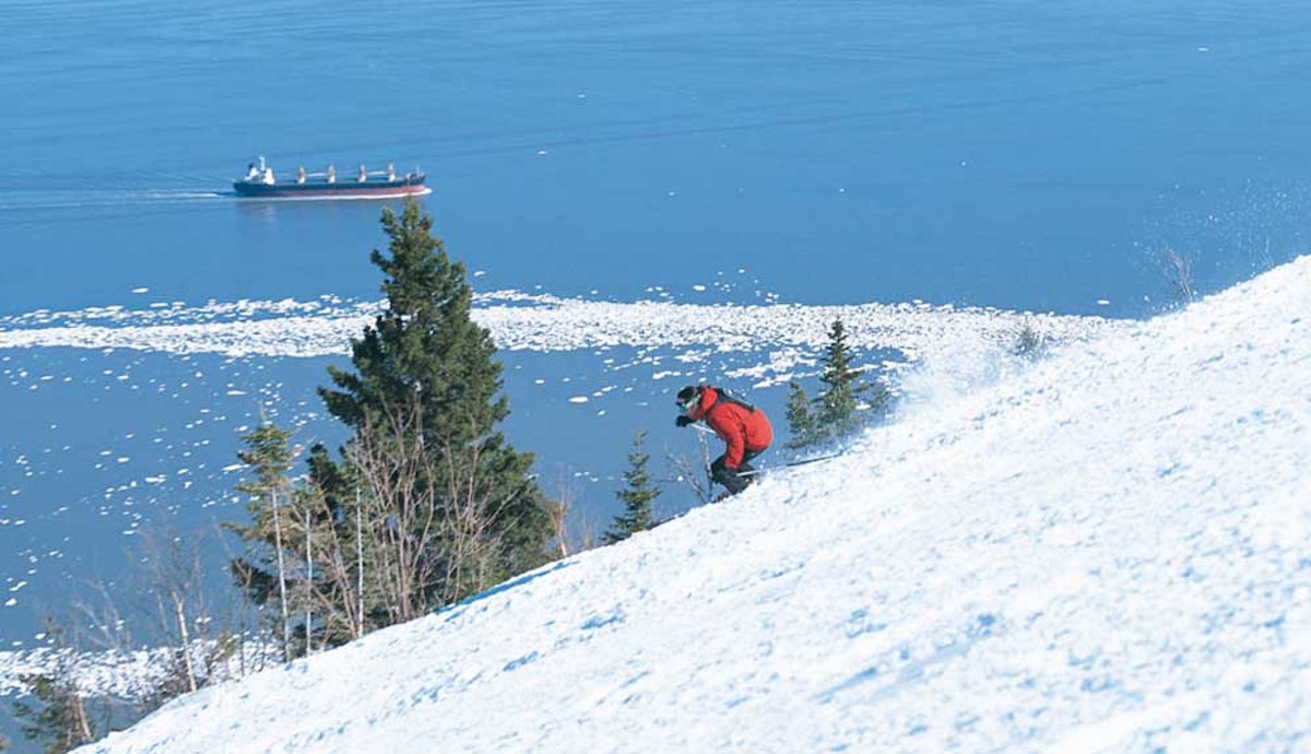 A person skiing down a snowy slope with a ship in the background.