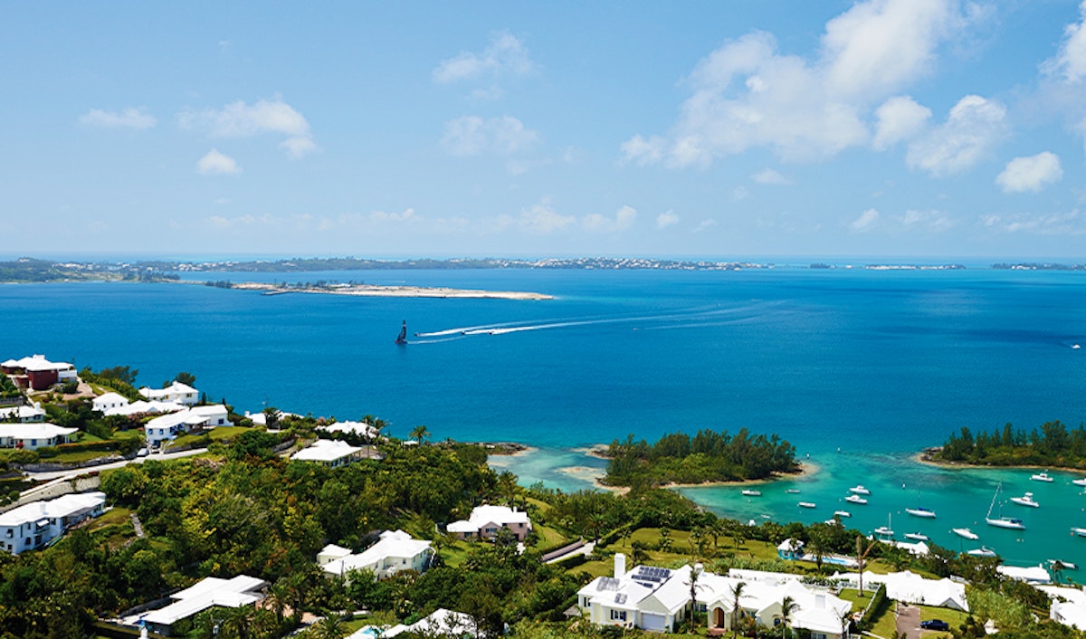 A panoramic view of a coastal region with clear blue waters, boats, and waterfront residences under a bright blue sky.