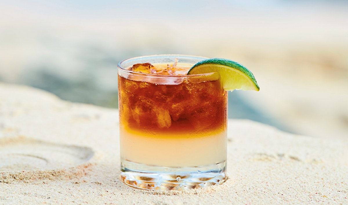 A glass of iced drink with a lime garnish on a sandy beach.