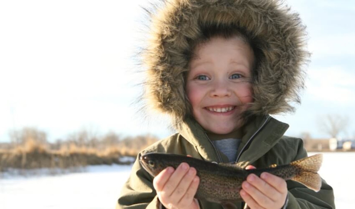 A young boy holding a fish in the snow.