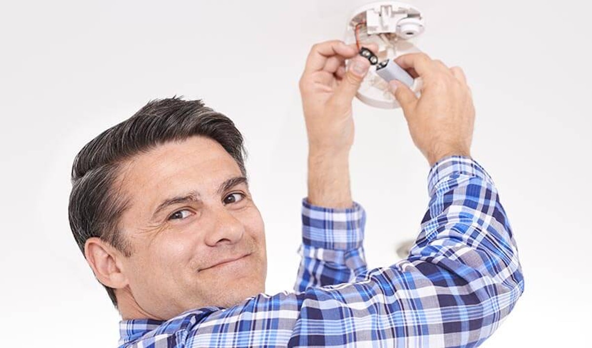 A man fixing a light fixture on a ceiling.