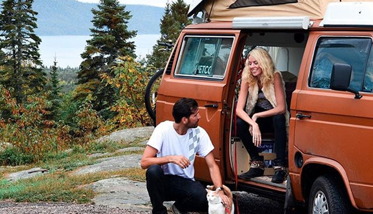 A man and woman sitting next to a vw camper van.