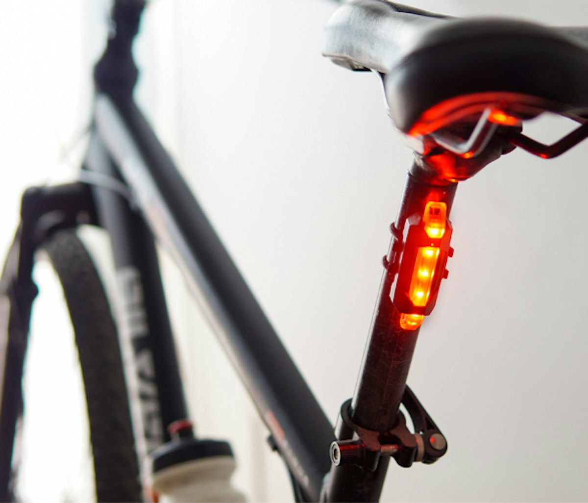 Rear view of a bicycle showing a seat and illuminated red tail light.