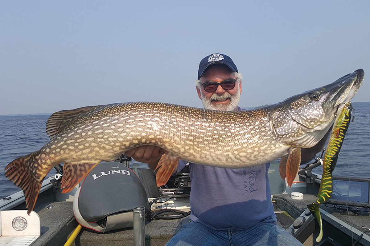 A man holding a large pike on a boat.