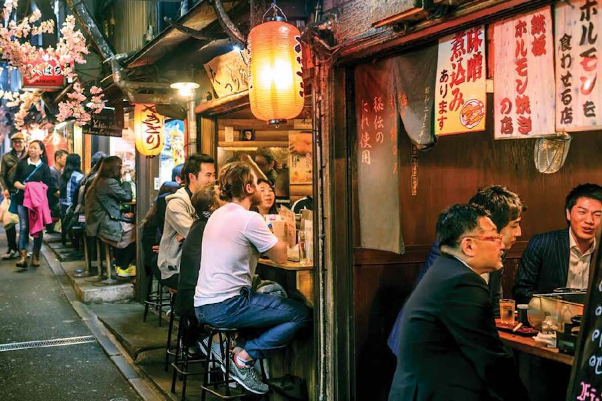 A group of people sitting at a bar in a narrow alley.