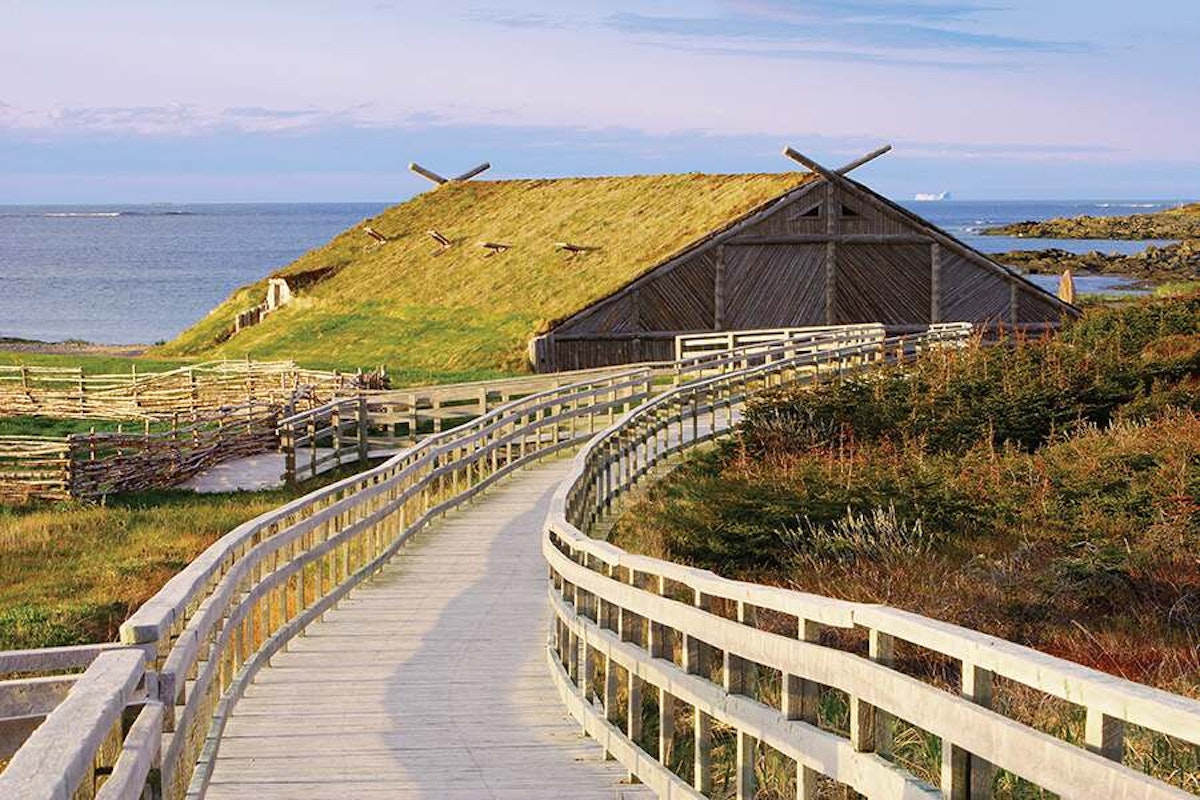 A wooden walkway leading to a grass roofed building.