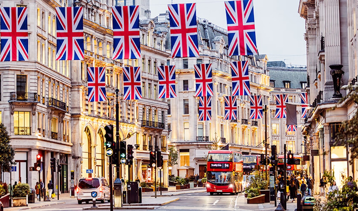 A street in the uk adorned with union jack flags, with a red double-decker bus in view.