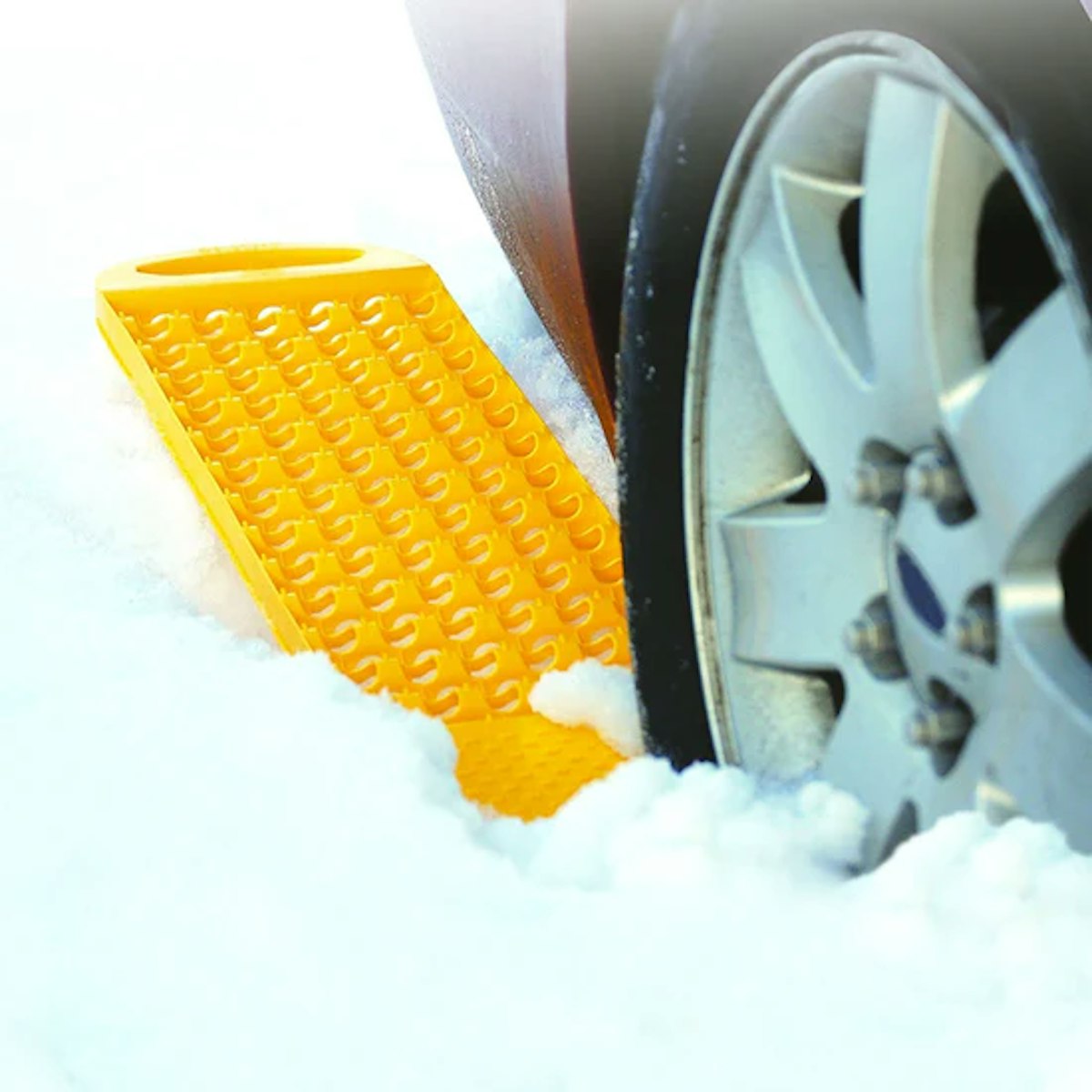 A yellow snow shovel next to a car in the snow.