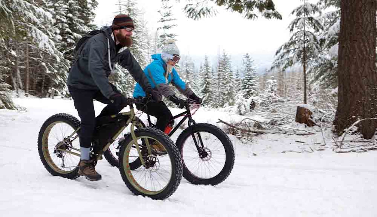 Two people riding bikes in the snow.